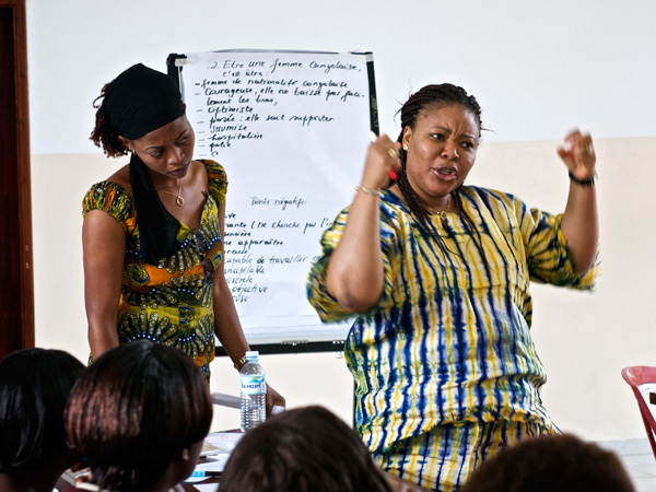 Nobel Peace Prize winner Leymah Gbowee stands in front of a white board with her hands raised like she's trying to push the crowd into action.