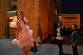 Man in swan dress stands outside with friends smoking