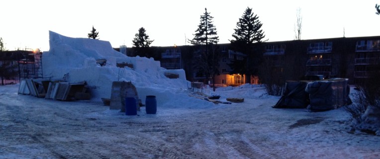 A snowy, muddy field leads up to a castle of snow at dusk.
