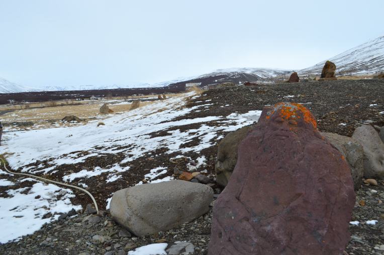 A massive boulder is carved into the shape of a contented man with closed eyes. It sits in a field of stone and snow.