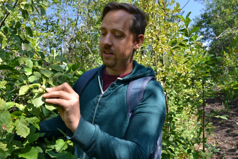Dustin holds up a leaf, with many trees behind him